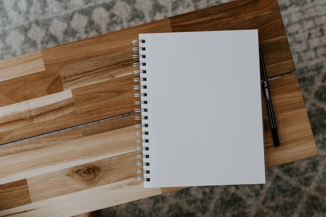 Åpen, blank spiralnotatbok og svart penn på et trebord